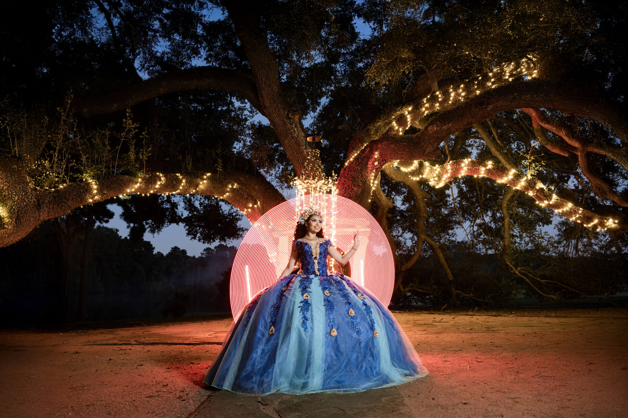 Dramatic night portrait of quinceañera in blue dress under lit trees – Cabrera Photography Quinceañera